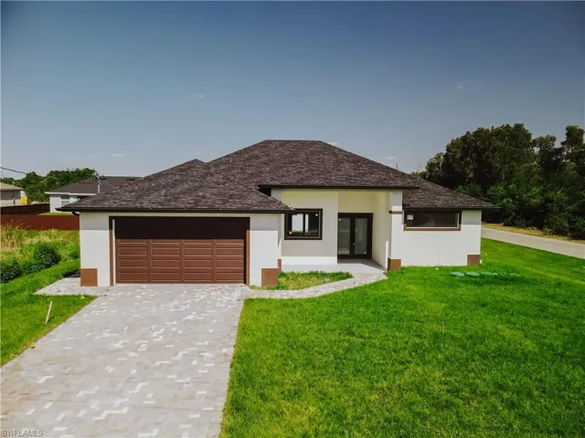Prairie-style house with a front yard, a garage, stucco siding, decorative driveway, and roof with shingles