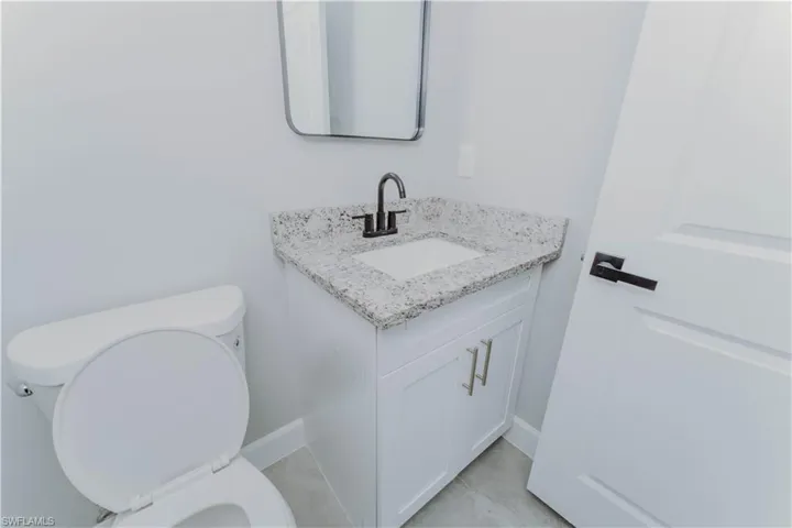 Bathroom featuring toilet, vanity, baseboards, and tile patterned flooring