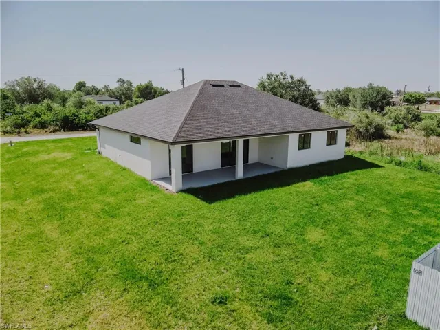 Back of house featuring a yard, a shingled roof, a patio, and stucco siding