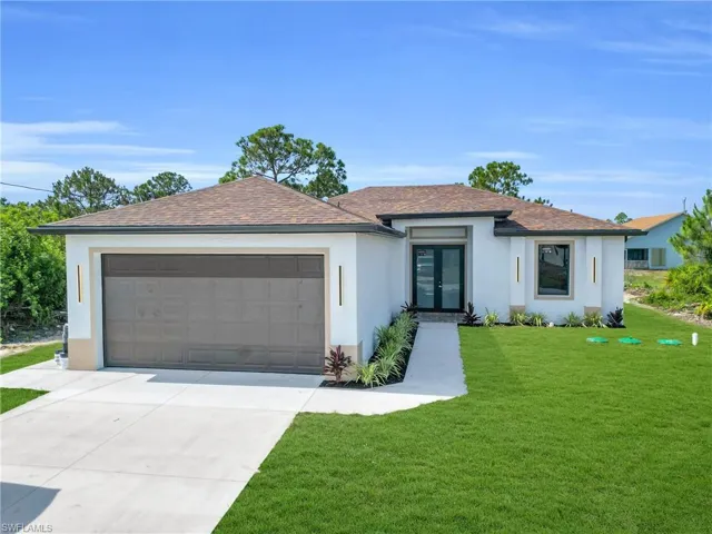 View of front facade with french doors, stucco siding, an attached garage, driveway, and a front lawn