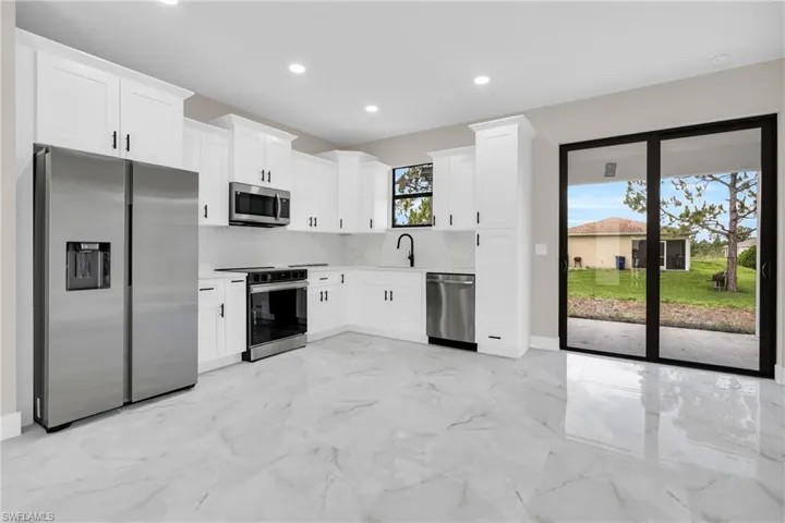 Kitchen with stainless steel appliances, recessed lighting, backsplash, white cabinets, and light marble finish floors