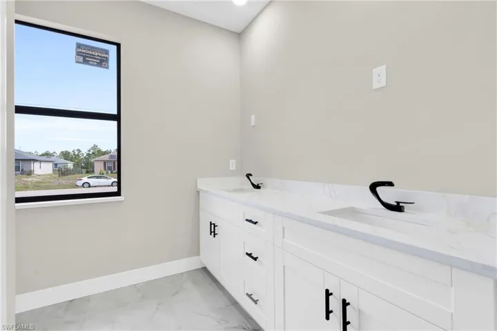 Bathroom with marble look tile flooring, baseboards, and double vanity