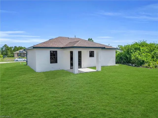 Rear view of house featuring a patio area, a lawn, and stucco siding
