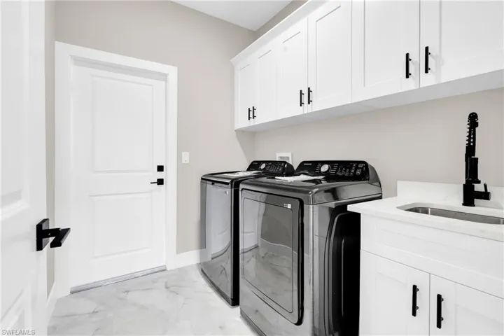 Washroom featuring washer and dryer, light marble finish flooring, cabinet space, and baseboards