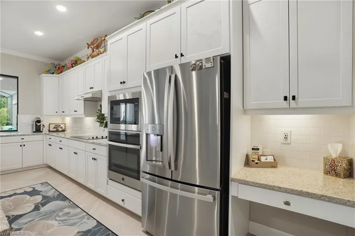 Kitchen with stainless steel appliances, tasteful backsplash, under cabinet range hood, crown molding, and white cabinets