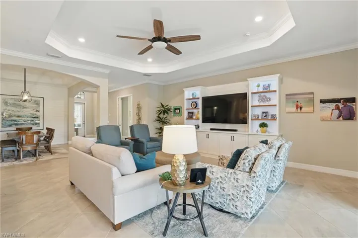 Living room featuring a raised ceiling, a ceiling fan, arched walkways, light tile patterned flooring, and ornamental molding