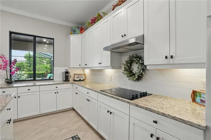 Kitchen featuring black electric stovetop, under cabinet range hood, white cabinetry, ornamental molding, and backsplash