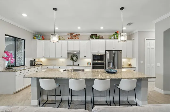 Kitchen featuring stainless steel appliances, a sink, under cabinet range hood, a large island, and white cabinetry