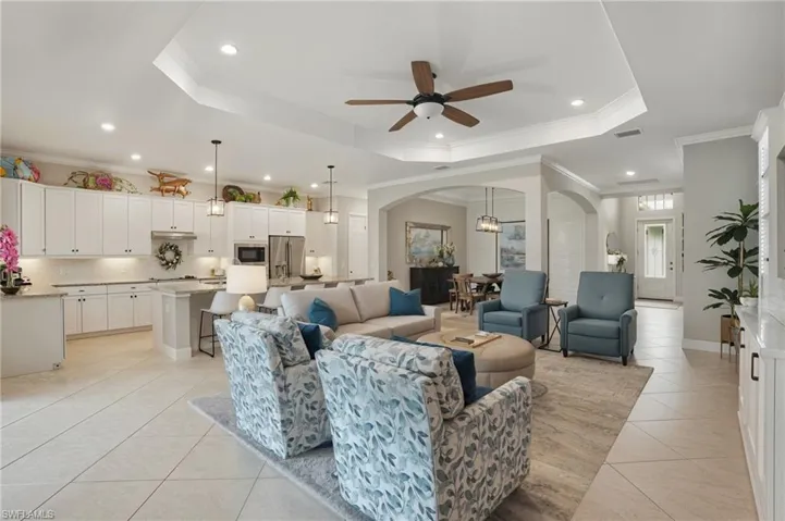 Living room with arched walkways, a raised ceiling, light tile patterned floors, a ceiling fan, and recessed lighting