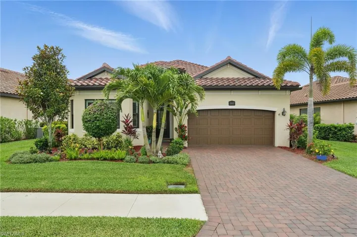 Mediterranean / spanish-style home featuring an attached garage, stucco siding, a tile roof, a front yard, and decorative driveway