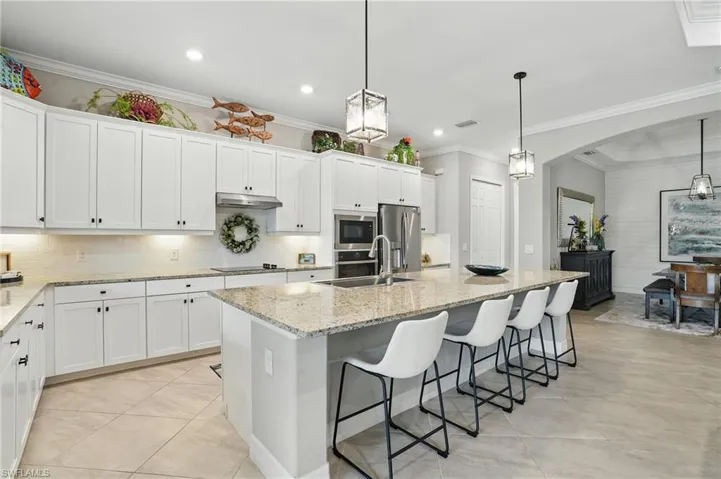 Kitchen featuring a sink, stainless steel appliances, a center island with sink, arched walkways, and white cabinetry