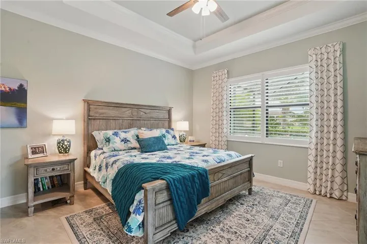 Bedroom with light tile patterned flooring, ornamental molding, baseboards, a raised ceiling, and a ceiling fan