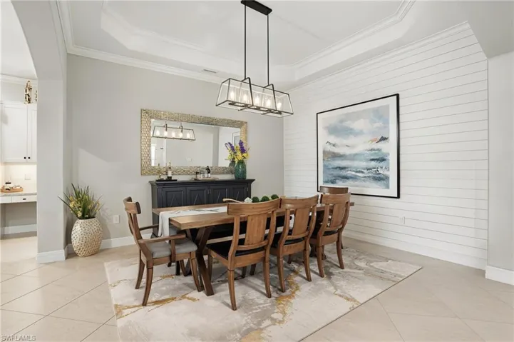 Dining room featuring light tile patterned floors, a chandelier, wood walls, ornamental molding, and a raised ceiling