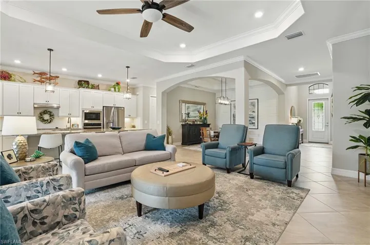 Living area with arched walkways, a ceiling fan, light tile patterned flooring, ornamental molding, and baseboards