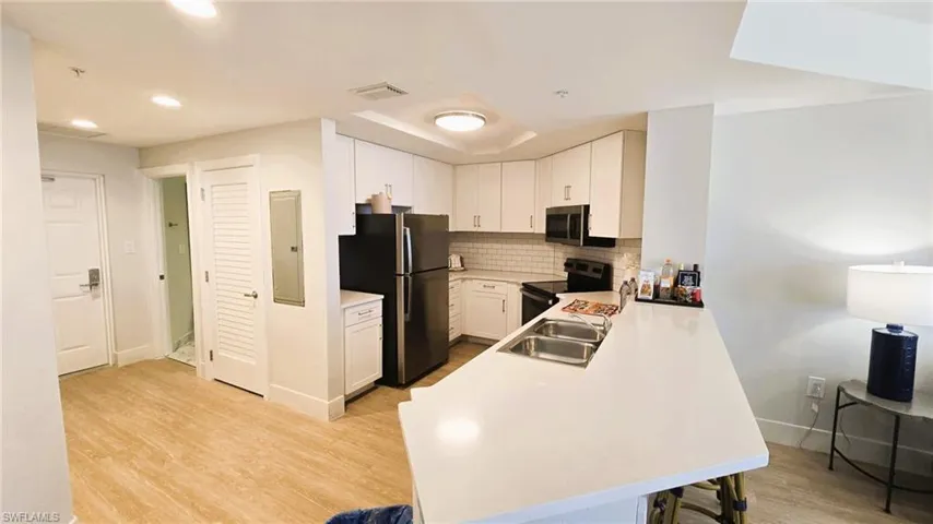 Kitchen with light countertops, decorative backsplash, white cabinetry, light wood-type flooring, and a peninsula