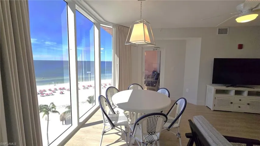 Dining space with wood finished floors, a beach view, floor to ceiling windows, and a ceiling fan