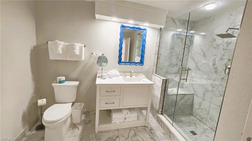 Bathroom with a marble finish shower, a textured wall, light marble finish floors, and vanity
