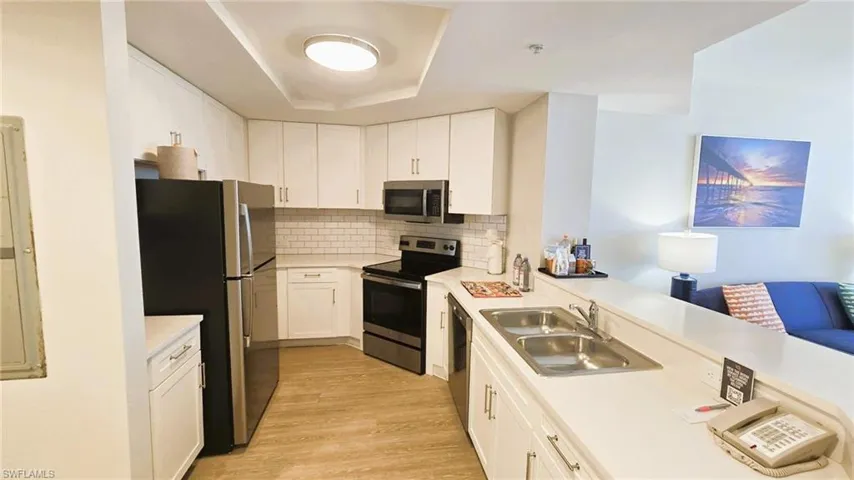 Kitchen with stainless steel appliances, decorative backsplash, white cabinets, and light wood-style flooring
