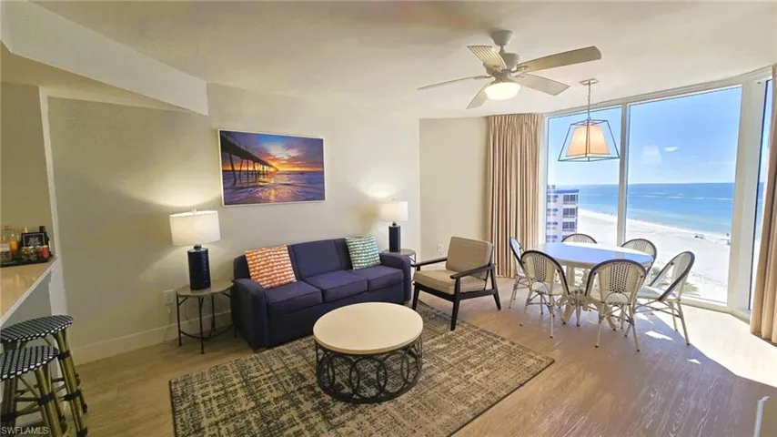Living room with a wall of windows, wood finished floors, view of water and beach, and ceiling fan