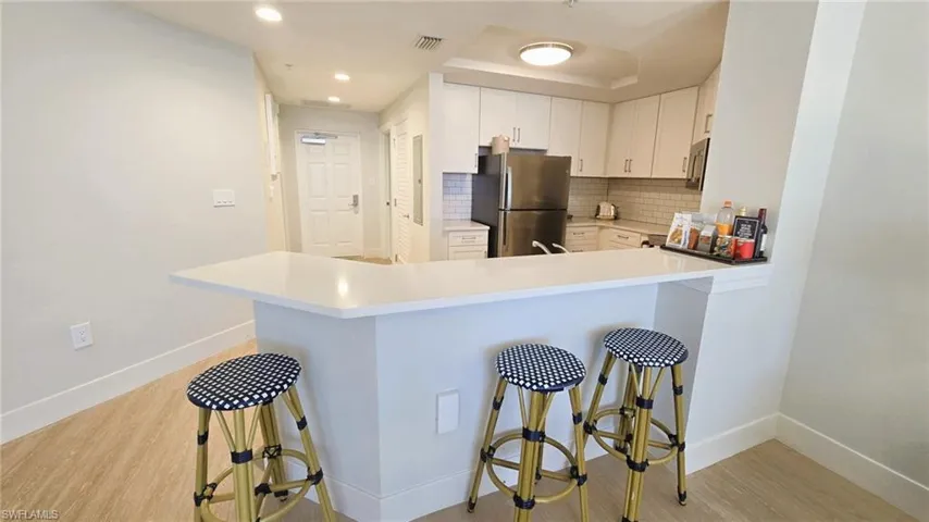 Kitchen featuring backsplash, light wood-style floors, a kitchen bar, appliances with stainless steel finishes, and light countertops