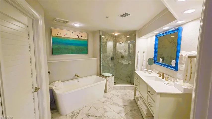 Full bathroom with vanity, a marble finish shower, a freestanding bath, light marble finish floors, and recessed lighting