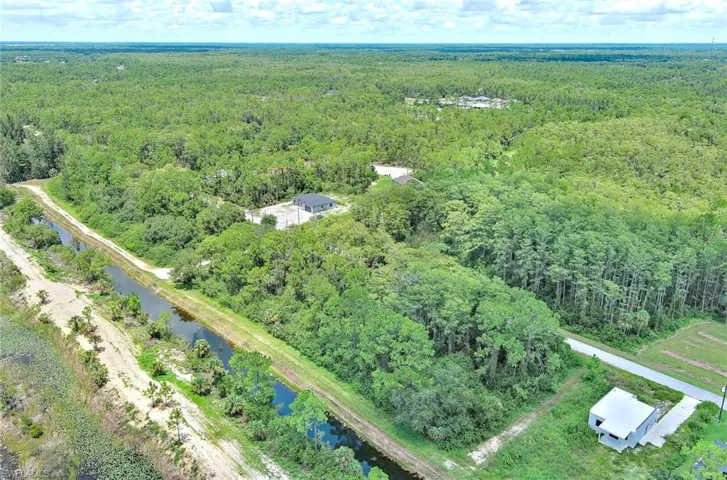 Aerial overview of property's location featuring a forest and a nearby body of water