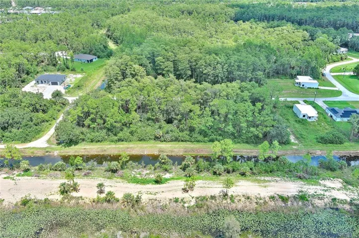Aerial view of property and surrounding area featuring a forest and a nearby body of water