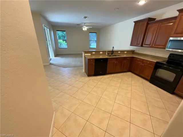 Kitchen with light tile patterned flooring, kitchen peninsula, ceiling fan, black appliances, and sink