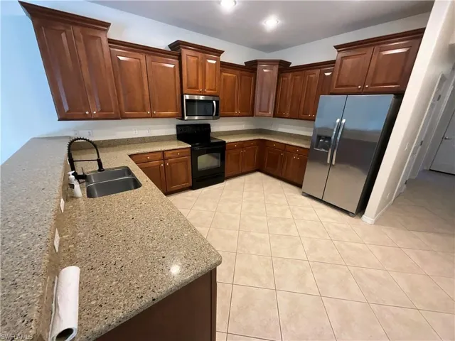Kitchen with sink, light tile patterned flooring, light stone countertops, and stainless steel appliances