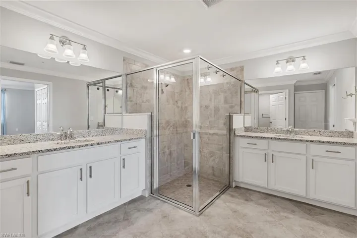 Bathroom featuring ornamental molding, a shower stall, two vanities, and recessed lighting