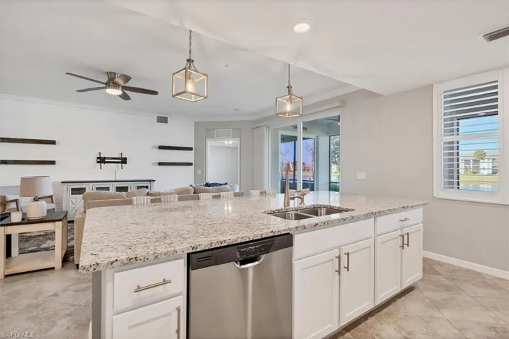 Kitchen with ceiling fan, white cabinetry, stainless steel dishwasher, hanging light fixtures, and light stone counters