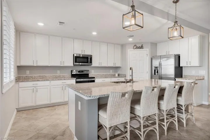 Kitchen featuring stainless steel appliances, a kitchen breakfast bar, light stone countertops, and white cabinets