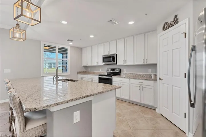 Kitchen featuring white cabinetry, stainless steel appliances, hanging light fixtures, and light stone countertops
