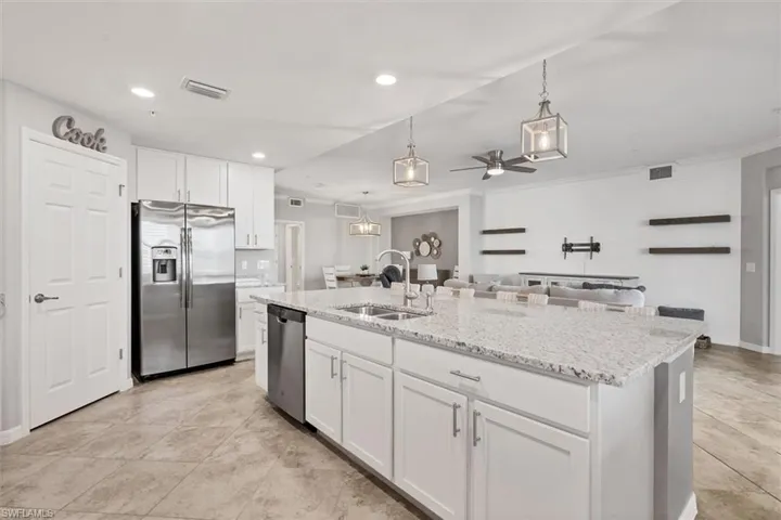 Kitchen featuring white cabinets, light stone counters, stainless steel appliances, decorative light fixtures, and a kitchen island with sink