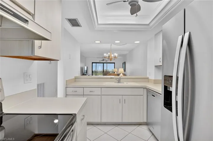 Kitchen with stainless steel appliances, light countertops, hanging lights, a tray ceiling, and light tile patterned flooring
