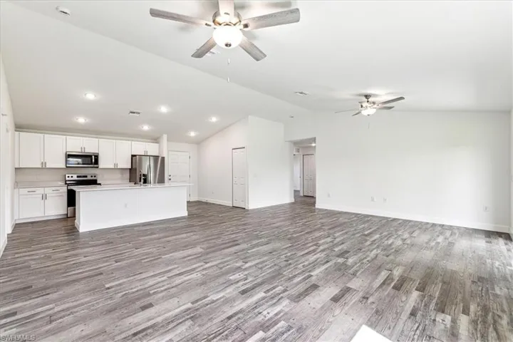 Kitchen with lofted ceiling, a kitchen island with sink, stainless steel appliances, light wood-type flooring, and white cabinets