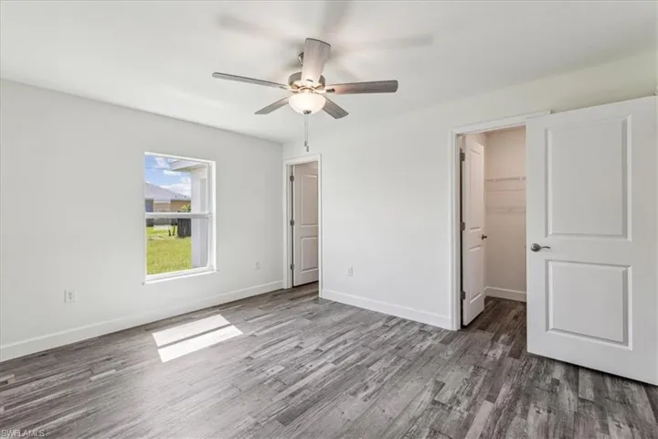 Unfurnished bedroom featuring dark wood-type flooring, a walk in closet, a closet, and ceiling fan