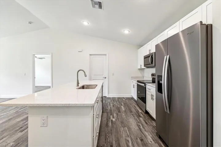 Kitchen with appliances with stainless steel finishes, sink, lofted ceiling, white cabinets, and a kitchen island with sink