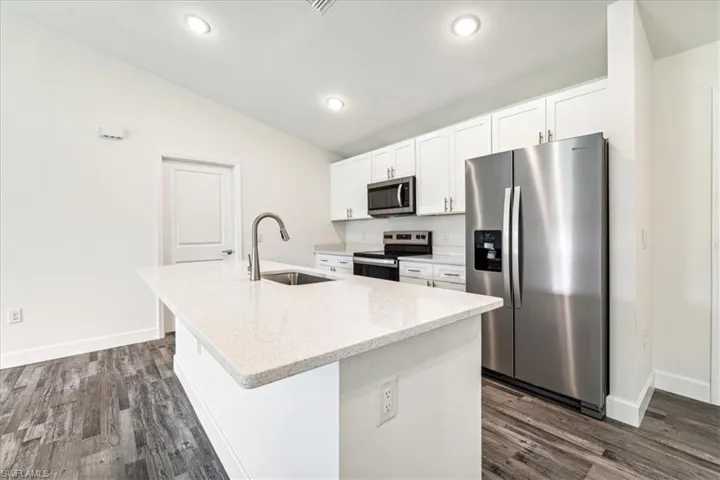 Kitchen featuring a kitchen island with sink, stainless steel appliances, sink, vaulted ceiling, and light stone counters