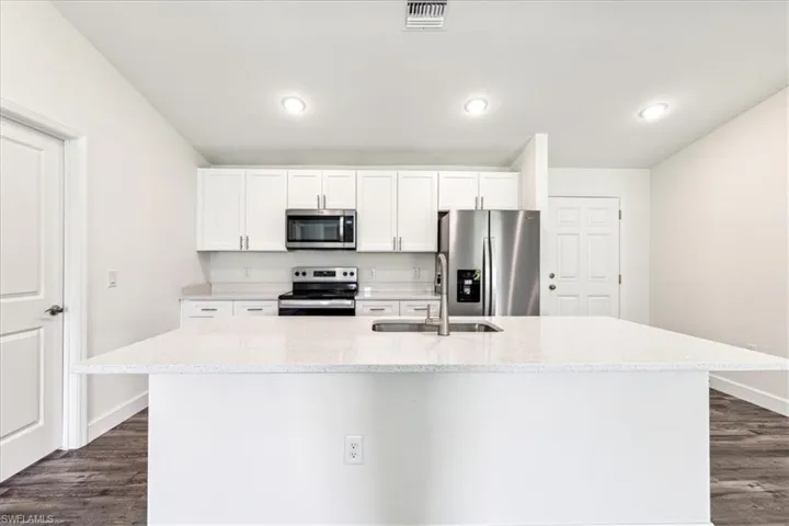 Kitchen featuring white cabinetry, appliances with stainless steel finishes, sink, and an island with sink