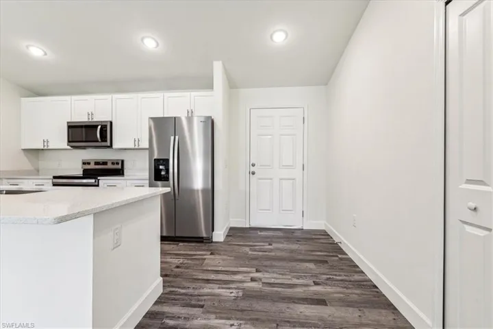 Kitchen with appliances with stainless steel finishes, dark hardwood / wood-style floors, and white cabinetry