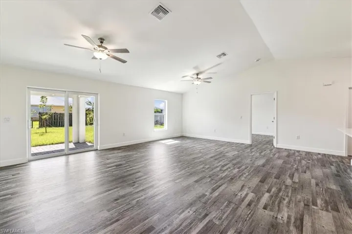 Spare room featuring ceiling fan, dark wood-type flooring, vaulted ceiling, and a wealth of natural light