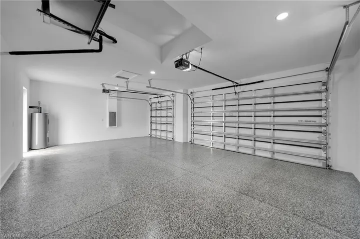 Garage with water heater, a garage door opener, electric panel, and recessed lighting