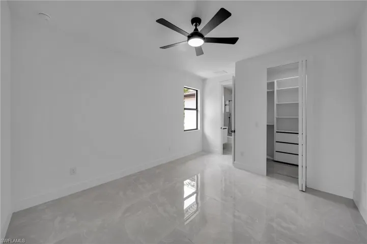 Unfurnished bedroom with a spacious closet, marble finish floor, and baseboards