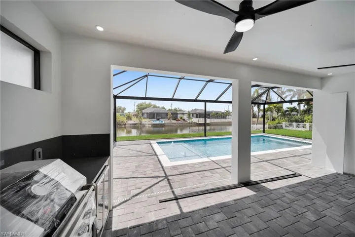 Pool featuring glass enclosure, ceiling fan, a water view, and a patio area