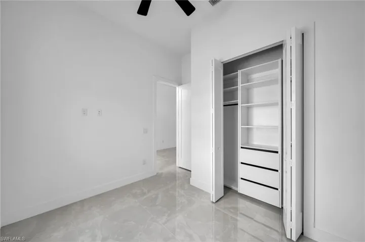 Unfurnished bedroom with a closet, marble finish floor, baseboards, visible vents, and ceiling fan