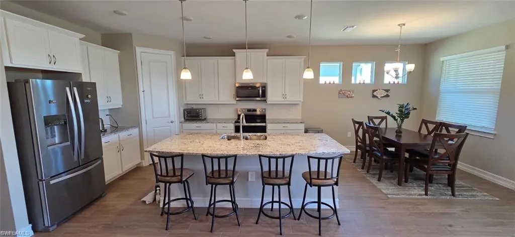 Kitchen with stainless steel appliances, white cabinetry, light stone countertops, a kitchen breakfast bar, and a kitchen island with sink