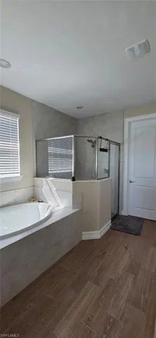 Full bathroom featuring a walk in shower, a garden tub, and dark wood finished floors