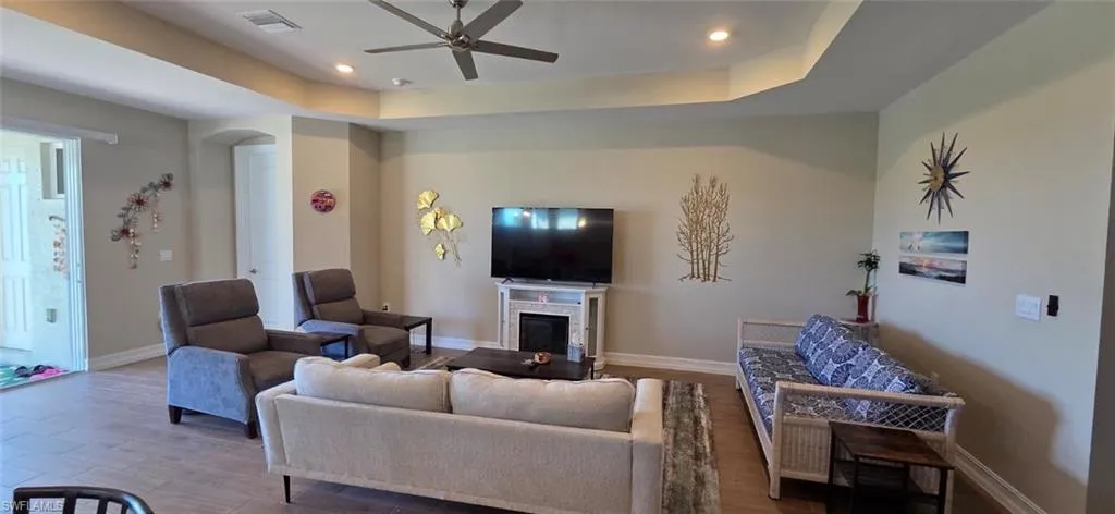 Living room featuring ceiling fan, recessed lighting, wood finished floors, a fireplace, and a tray ceiling