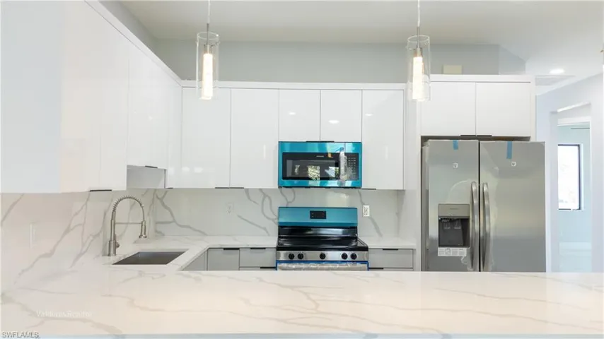 Kitchen featuring light stone counters, appliances with stainless steel finishes, white cabinets, decorative light fixtures, and modern cabinets